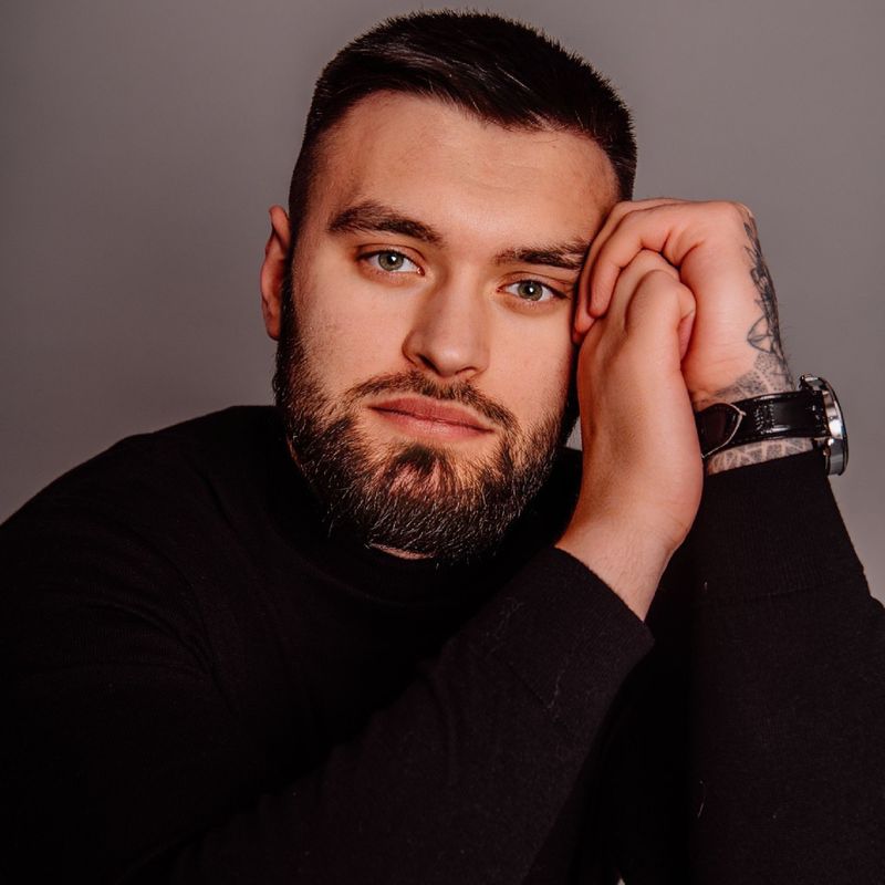 Portrait of a bearded man resting his head on hands, showcasing a thoughtful expression in a studio setting.